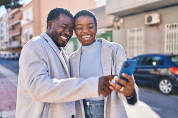 Man and woman couple standing together using smartphone at street