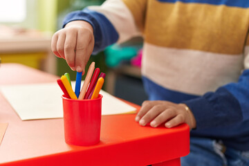 Adorable hispanic boy preschool student sitting on table holding pencil at kindergarten