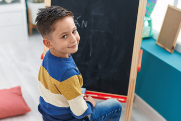 Adorable hispanic boy preschool student drawing on blackboard at kindergarten