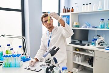 Naklejka premium Young hispanic man scientist holding test tube write on document at laboratory