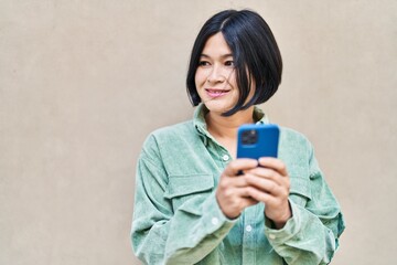 Young chinese woman smiling confident using smartphone at street