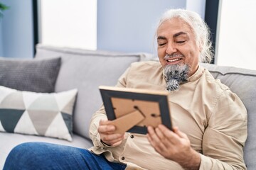 Fototapeta premium Middle age grey-haired man looking picture sitting on sofa at home