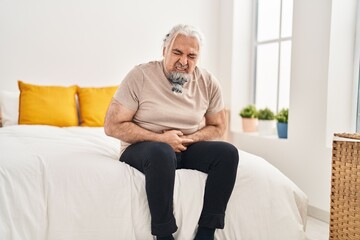 Middle age grey-haired man suffering for stomach ache sitting on bed at bedroom