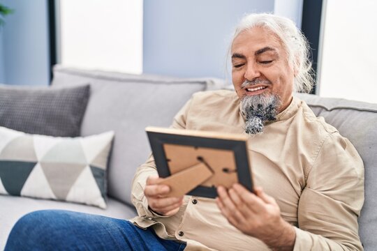 Middle age grey-haired man looking picture sitting on sofa at home