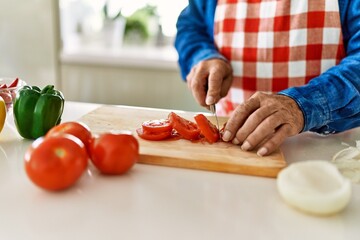 Obraz na płótnie Canvas Senior man cutting tomato at kitchen