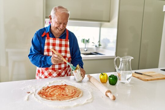 Senior man smiling confident cooking pizza at kitchen