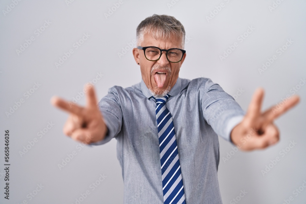 Canvas Prints Hispanic business man with grey hair wearing glasses smiling with tongue out showing fingers of both hands doing victory sign. number two.