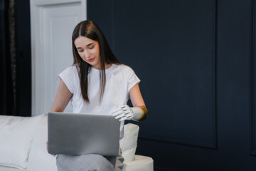 Brunette caucasian girl in casual sitting on sofa at home using bionic arm prosthesis, opens...