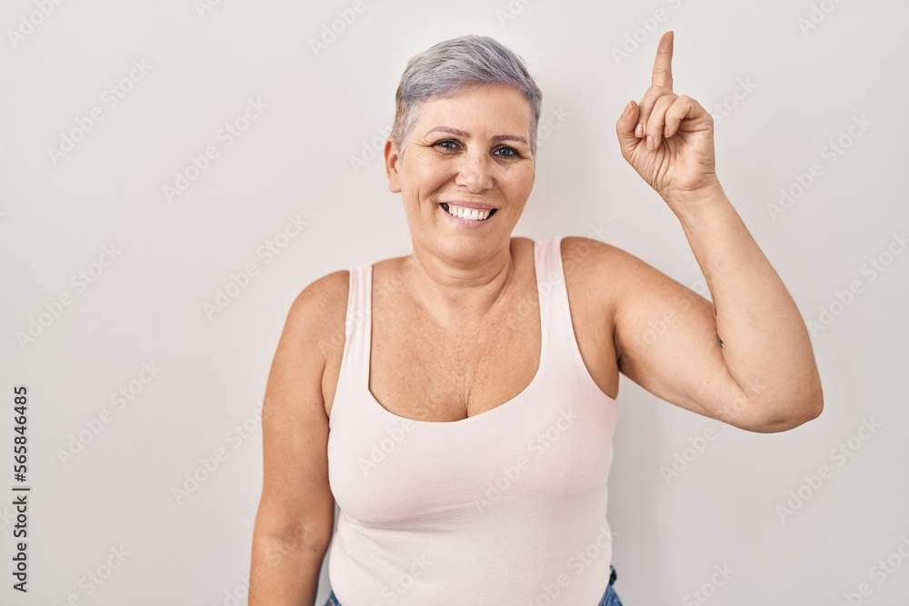 Sticker middle age caucasian woman standing over white background pointing finger up with successful idea. e