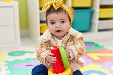 Adorable blonde toddler sitting on floor holding hoop toy at kindergarten