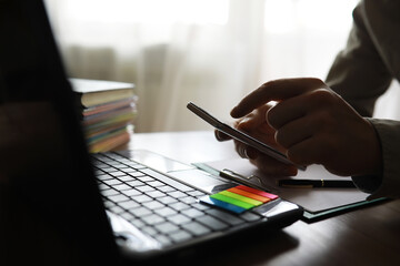 Hands using laptop and phone for online shopping, close up clean image in front of the window in soft light