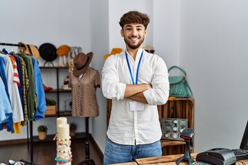 Young arab man shopkeeper smiling confident with arms crossed gesture at clothing store