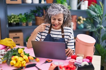Middle age woman with grey hair working at florist with laptop smiling happy pointing with hand and finger