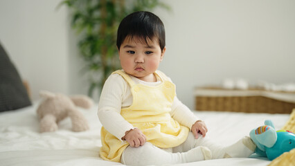 Fototapeta premium Adorable hispanic baby playing with elephant doll sitting on bed at bedroom