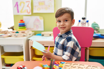 Adorable hispanic boy student smiling confident cutting paper at kindergarten