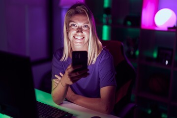 Young blonde woman streamer using computer and smarpthone at gaming room