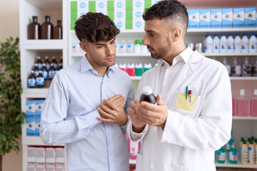 Two hispanic men pharmacist speaking to client showing medication label bottle at pharmacy