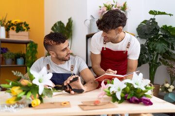 Two hispanic men florists cutting stem of flower writing on notebook at flower shop