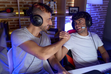 Two hispanic men streamers playing video game shake hands at gaming room