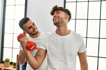 Two hispanic men couple smiling confident training using dumbbell at home