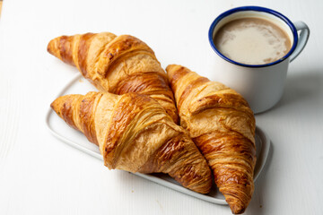 Top view of three croissants on white plate on white table and cup of latte, horizontal, with copy space