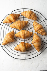 Overhead view of small croissants on black rack and white table, vertically, with copy space