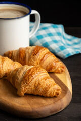 Close-up of small croissants on wood with cup of coffee and blue cloth, table and dark background, vertical, with copy space