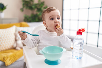 Adorable caucasian baby sitting on highchair eating biscuit at home