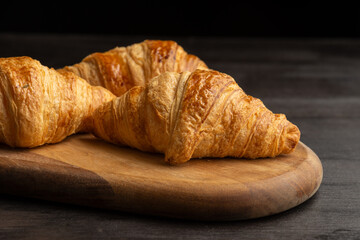 Close up of golden croissants on wooden board over table and dark background in landscape, with copy space