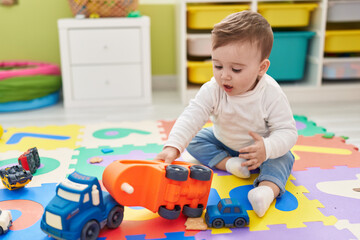 Adorable caucasian baby playing with truck toy sitting on floor at kindergarten