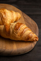 Top view of golden croissants on wooden board and dark table, vertical, with copy space