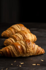 Top view of golden croissants on dark table and black background, vertical, with copy space