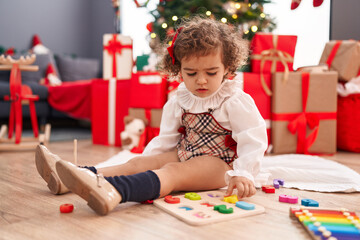 Adorable hispanic girl playing with maths game sitting on floor by christmas tree at home