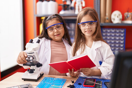 Two kids students using microscope reading notebook at laboratory classroom