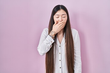 Chinese young woman standing over pink background bored yawning tired covering mouth with hand. restless and sleepiness.
