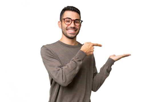 Young handsome caucasian man over isolated background holding copyspace imaginary on the palm to insert an ad
