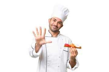 Young caucasian chef holding a sushi over isolated background counting five with fingers