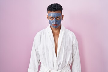 Young hispanic man wearing beauty face mask and bath robe depressed and worry for distress, crying angry and afraid. sad expression.