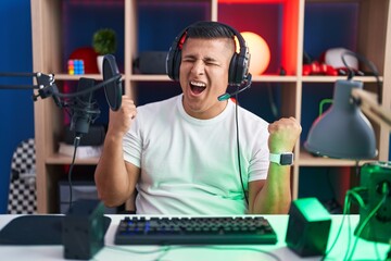 Young hispanic man playing video games very happy and excited doing winner gesture with arms raised, smiling and screaming for success. celebration concept.