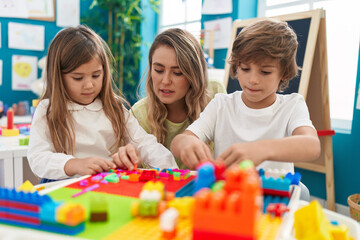 Teacher with boy and girl playing with construction blocks sitting on table at kindergarten