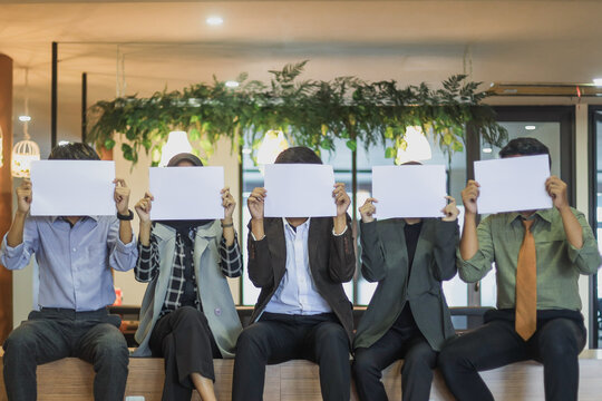 Group Of Unrecognizable Young Multiracial Business People Covering Faces Hiding Behind Blank Mockup Signs. Team Of Anonymous Multiethnic Office Workers Holding Empty White Sheets Of Paper.