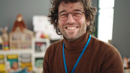 Young hispanic man preschool teacher smiling confident standing at kindergarten