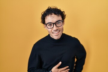 Fototapeta premium Hispanic man standing over yellow background smiling and laughing hard out loud because funny crazy joke with hands on body.