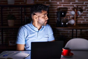 Fototapeta na wymiar Hispanic man with beard using laptop at night looking to side, relax profile pose with natural face with confident smile.