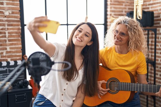 Two women musicians playing classical guitar making selfie by smartphone at music studio