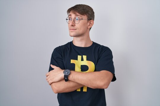Caucasian blond man wearing bitcoin t shirt looking to the side with arms crossed convinced and confident