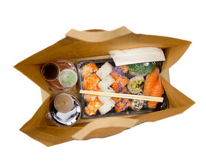 Sushi to go concept. Top view of takeaway box with sushi rolls and various sauce cups in brown...