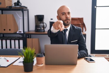 Middle age bald man working at the office pointing with finger to the camera and to you, confident gesture looking serious