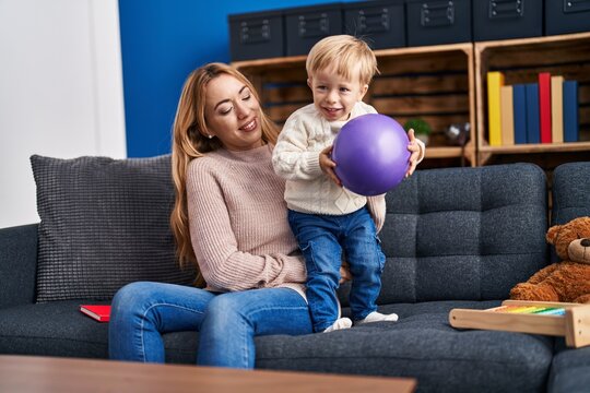 Mother and son playing with ball sitting on sofa at home