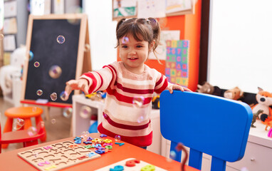 Adorable hispanic girl smiling confident playing with bubbles at kindergarten